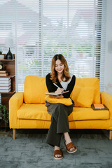 Obraz premium Attractive young asian woman leaning of sofa, reading a novel book