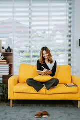 Portrait young asian woman read book on sofa chair with pillow in living room