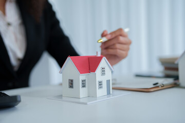 An African American female real estate agent presents a house model to a client, discussing...