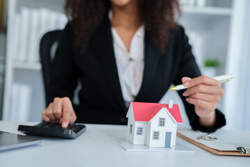 An African American female real estate agent presents a house model to a client, discussing mortgage loan contracts, home purchase agreements, and home insurance policies