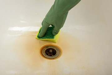 Man or woman in green gloves cleans bathroom from yellow stains from hard water