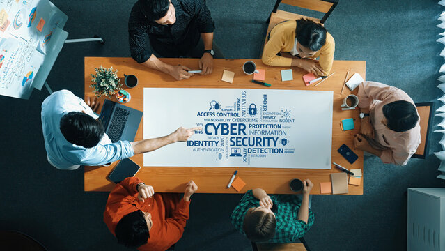 A diverse team discusses cybersecurity strategies at a meeting, focusing on access control, identity protection, and information security solutions with various tools and notes. Amity