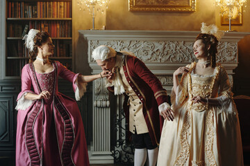 Caucasian middle aged man wearing Baroque period costume bowing and kissing hand of Caucasian young...