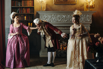 Caucasian middle aged man bowing and kissing hand of Caucasian middle aged woman in ornate Baroque...