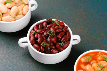 Three types of cooked beans in white bowls on textured table for vegan diet, nutrition or protein food concept