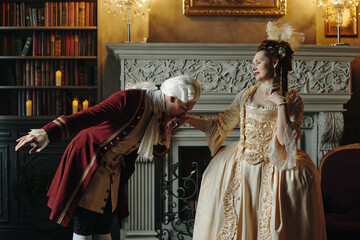 Man in Baroque costume bowing and kissing hand of Caucasian middle aged woman in ornate Renaissance...