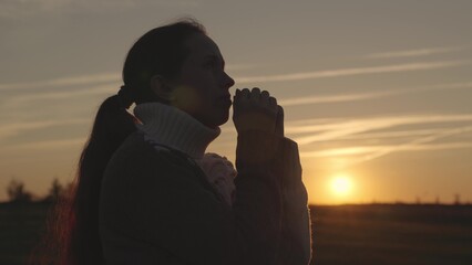 girl praying at sunset in the sky, silhouette of a woman asking for help, reading prayer in sun,...