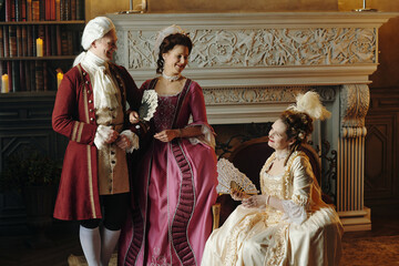 Caucasian middle aged man and two Caucasian middle aged women wearing Baroque period costumes...