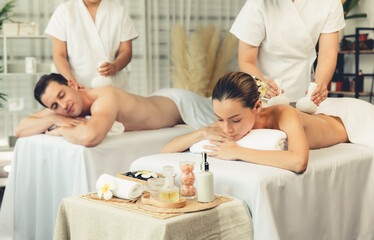 Hot herbal ball spa massage body treatment, masseur gently compresses herb bag on couple customer...