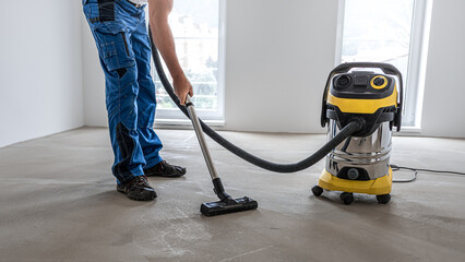 Floating floor work. A worker vacuums the floor before laying the vinyl floor layer.