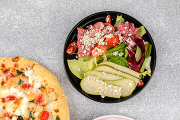 Pear salad and pizza on gray surface for vegetarian and restaurant food concept