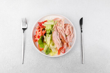 Protein salad with turkey, cheese and vegetables in white bowl with cutlery for fitness meal plan...