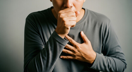 A man coughing into his hand covering his mouth and chest suggesting illness or discomfort against a plain background