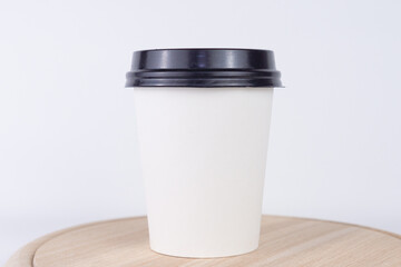 A white disposable coffee cup with a black lid, on a plain white background, concept of coffee breaks, convenience, and daily routines.
