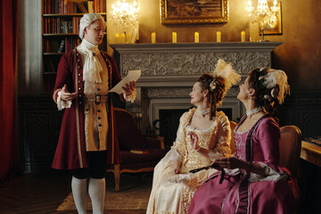 Caucasian middle aged man standing and reading document to two seated Caucasian young adult women...