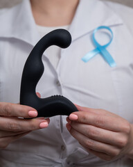 Female doctor holding prostate massager and blue ribbon. Symbol of fight against prostate cancer. 