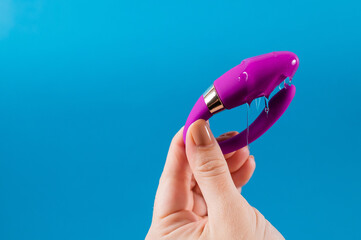 A woman holds a curved sex toy in lubrication on a blue background. Vaginally clitoral vibrator. 