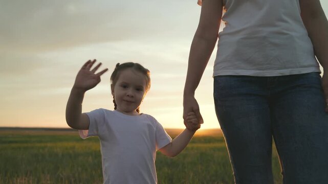 Mom leads little girl by hand, waving her hand in the glare of the sunset, a dream to be a happy family, close-up of a smiling child, hold a child's hand in an older hand, motherly love and care kid,