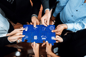 Diverse hands collaboratively assemble a puzzle featuring icons symbolizing business strategies,...