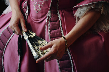Caucasian middle aged woman holding ornate hand fan while wearing elaborate Baroque style dress...