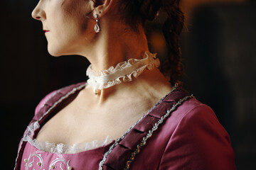 Caucasian middle aged woman wearing ornate dress and lace choker standing in profile with braided...