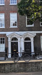 Facade of old brick victorian or gregorian house with classic black doors and wrought iron fence and bicycle