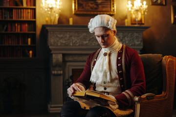 Caucasian young adult man wearing historical Baroque costume sitting in ornate room reading book,...