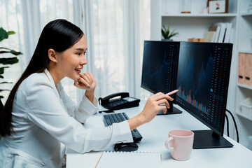 Young beautiful Asian businesswoman looking on pc to analyze profitable of exchange stock market...