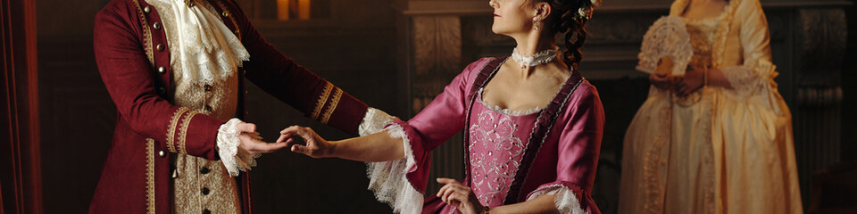 Caucasian middle aged man holding hand of Caucasian young adult woman wearing Baroque period...