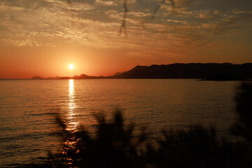 Golden sunset over the sea with glowing reflection on the water and silhouettes of distant hills....