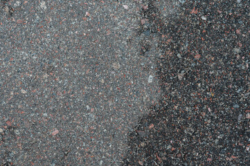 Close up view of a textured surface composed of small, multicolored stones. The stones are predominantly dark gray and black, with flecks of reddish brown and lighter gray throughout