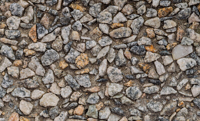 High angle close up view of a textured surface composed of small, multicolored stones embedded in a gray mortar. 