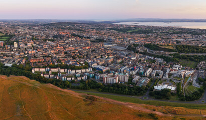 Panoramic Aerial image of the beautiful Edinburgh Cityscape featuring Holyrood Park touched by the first light of the morning Sunrise. 