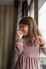 Playful child girl standing near the window in hotel room, childhood memories