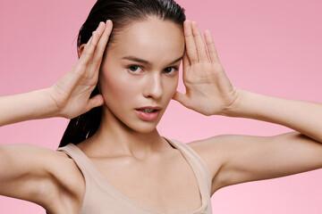 Young model with long hair posing against a soft pink background, expressing confidence and...