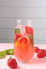 Refreshing drink with strawberries, mint and ice on pink wooden table against grey background, closeup