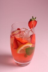Refreshing drink with strawberries, mint, lemon and ice in glass on pink background, closeup