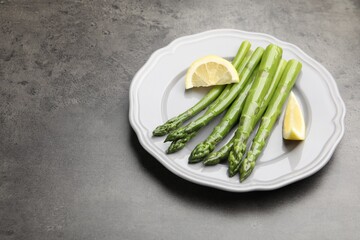 Tasty cooked asparagus served with lemon on grey table, space for text