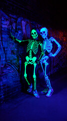 Fototapeta premium Glowing skeletons in a Halloween setting: Two illuminated skeletons pose in a dimly lit, textured environment, exuding a mysterious and slightly eerie ambiance, perfect for Halloween or themed events.
