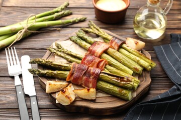 Tasty cooked asparagus served with bacon and sauce on wooden table, closeup