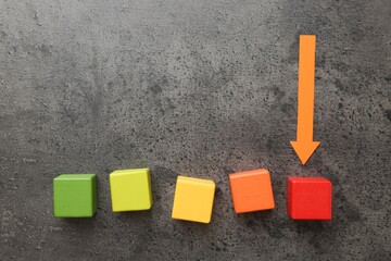 Maximum. Colorful cubes and arrow pointing at red one on grey table, flat lay