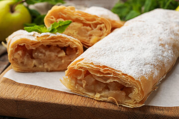 Tasty apple strudels with powdered sugar, mint and fruit on table, closeup