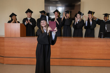 Happy Caucasian woman holds red diploma and classmates support her. 