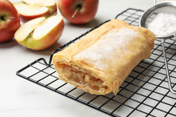 Tasty apple strudel with powdered sugar and fruits on white marble table, closeup