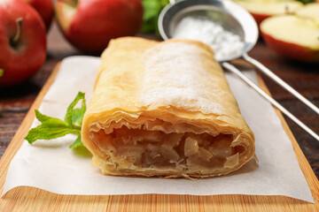 Tasty apple strudel with powdered sugar, mint and fruits on table, closeup