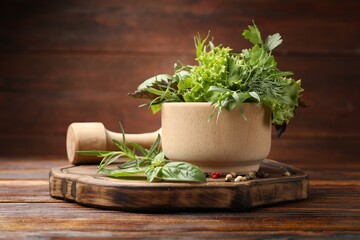 Mortar with pestle, different aromatic herbs and spices on wooden table