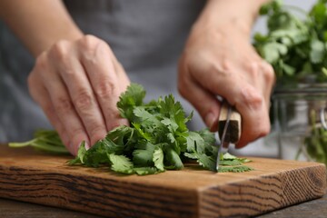 Woman cutting fresh cilantro at wooden table, closeup