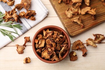 Dried chanterelle mushrooms in bowl and rosemary on light wooden table, flat lay