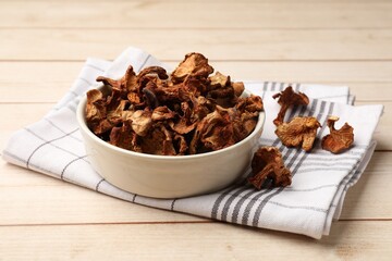 Dried chanterelle mushrooms in bowl on light wooden table, closeup