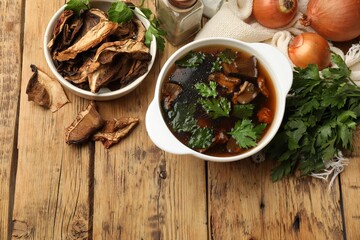 Tasty soup with mushrooms and parsley in bowl on wooden table, flat lay